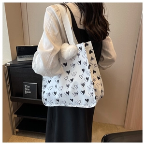 Close-up of white canvas tote bag with heart print and plush heart charm on a shoulder