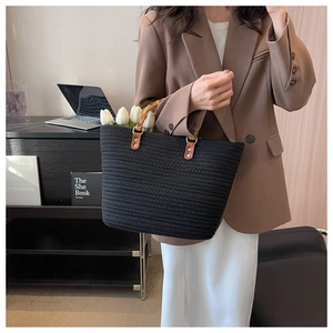 Detail of black woven tote bag featuring bamboo handles and premium leather patches