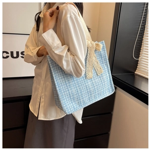 Detail of light blue tweed tote bag featuring a decorative cream lace bow and cotton strap
