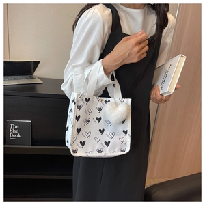Detail of white canvas tote bag with black heart pattern and plush heart pendant