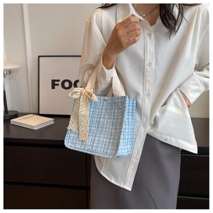 Detail of tweed tote bag with beige lace bow handle and blue woven texture