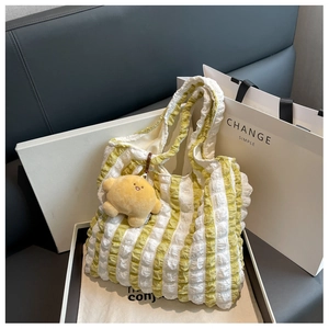 Detail of yellow striped seersucker tote bag with a soft plush ball charm and ruched texture