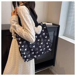 Detail of black canvas tote bag with heart patterns and plush charm on shoulder