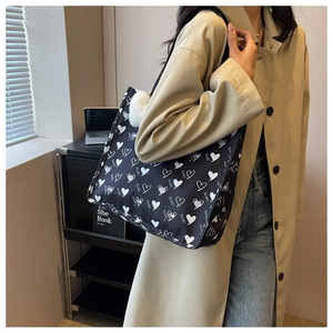 Detail of a large black canvas tote bag with heart pattern and white plush ball pendant