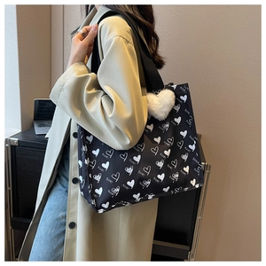 Detail of large black canvas tote bag with white heart print and plush heart charm