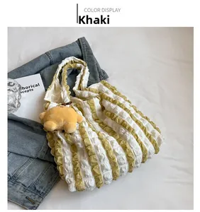 Close-up of khaki pleated cloud tote bag with a cute yellow bear plush keychain