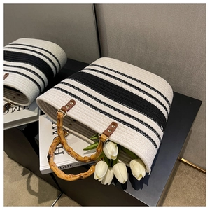 Detail of woven straw tote bag featuring black and white stripes and natural bamboo handles