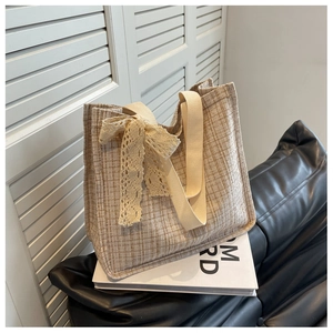 Close-up of beige woven canvas tote bag featuring lace bow detail and fabric strap