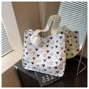 Detailed shot of white canvas tote bag with black heart pattern and plush ball accessory