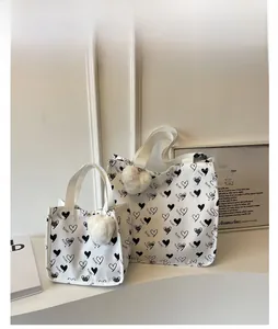 Detail of white canvas tote bag set with heart print and plush ball pendant charm