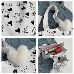 Detail view of large white canvas tote bag with black heart pattern and plush charm