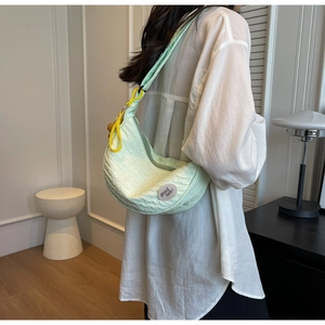 Close-up of light green quilted crescent bag with good luck label and yellow pendant