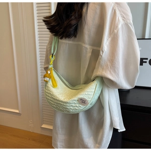 Detail of mint green crescent crossbody bag featuring pleated texture and bird charm