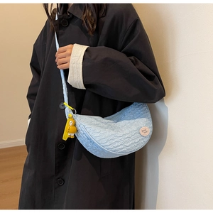 Close-up of light blue crescent canvas bag with pleat texture and duck pendant accessory