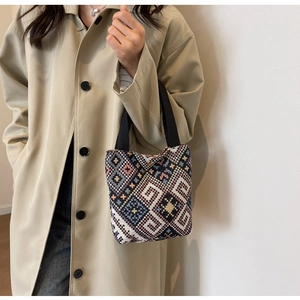 Detailed shot of ethnic woven handbag with geometric patterns held by a model in a trench coat