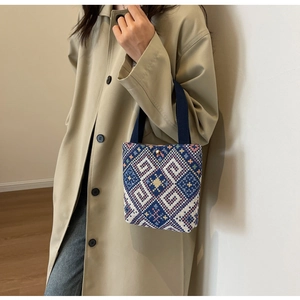 Close-up of bohemian geometric woven handbag with blue handles and gold metallic snap button