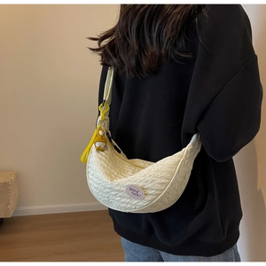 Close-up of cream pleated hobo bag with Good Luck patch and yellow charm on model