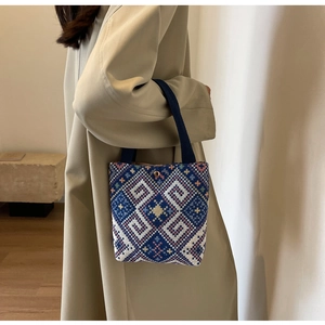Detail of ethnic geometric woven pattern on bucket bag with navy blue handle straps