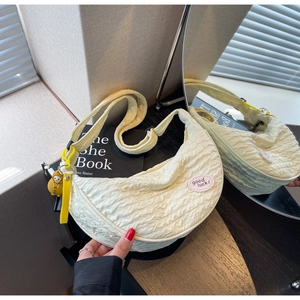 Detail of off-white pleated crescent bag with good luck label and duckling charm