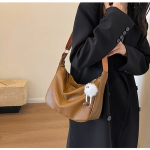 Close-up of brown pebbled leather crossbody bag with wide strap and plush monster charm