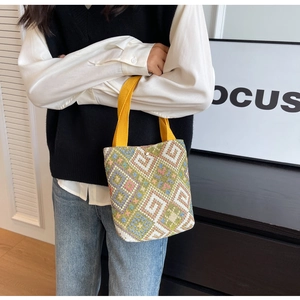 Detail of colorful geometric woven canvas bucket bag with yellow handle and pearl buckle