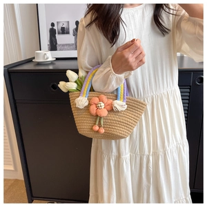 Detailed shot of handmade straw bag featuring a plush orange flower and rainbow woven handle