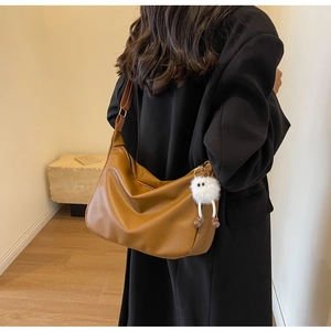 Detail of caramel soft leather hobo bag with wide strap and plush pendant on model