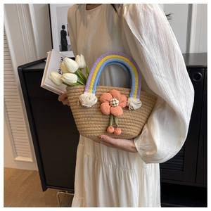 Detail of straw woven handbag featuring rainbow cotton rope handles and plush flower charm