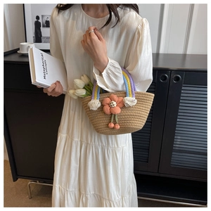 Detail of straw woven handbag featuring rainbow cotton handles and a pink floral accent