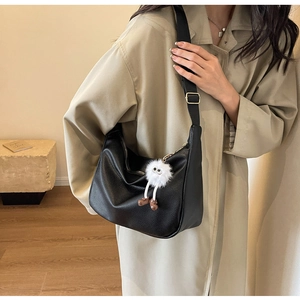 Detail of black textured leather hobo bag with a white plush monster charm and wide strap
