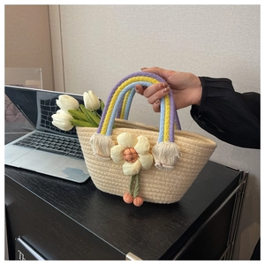 Detail of hand-woven straw basket bag featuring rainbow rope handles and floral charm