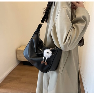 Close-up of black textured leather crossbody bag with cute white plush doll keychain