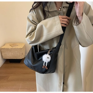 Lifestyle shot of black lychee leather crossbody bag with white plush doll charm
