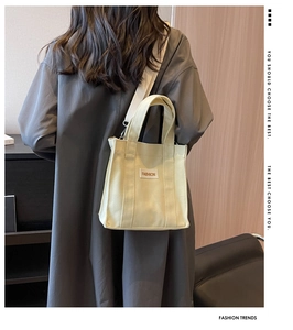 Minimalist beige canvas tote bag shown worn over a long trench coat for daily use