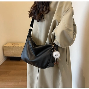 Detail of black lychee leather hobo bag with wide nylon strap and plush monster charm
