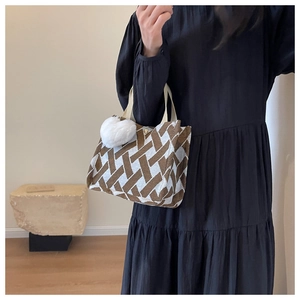 Detail of a large brown and white geometric pattern tote bag with a white plush pompom charm