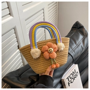 Close-up of woven straw basket bag with rainbow handle and large orange fabric flower