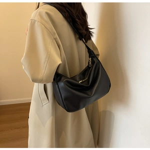 Model wearing a black lychee pattern leather crescent bag with golden hardware and wide strap