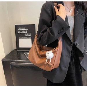 Close-up of brown textured leather crescent bag with a cute plush monster charm