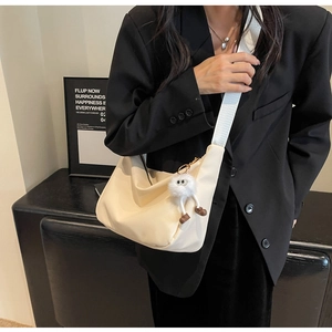 Chic cream leather hobo bag with wide strap and plush monster charm on model