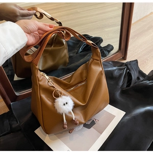 Detail of caramel lychee leather hobo bag with wide strap and funny plush eye charm