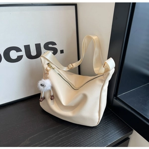 Detail of off-white leather hobo bag featuring litchi texture and white plush pendant