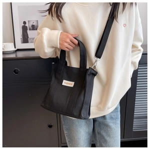 Detail shot of a black canvas crossbody bag with Fashion label worn by a model