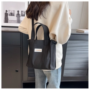 Detail view of black canvas tote bag with FASHION label worn as a shoulder bag