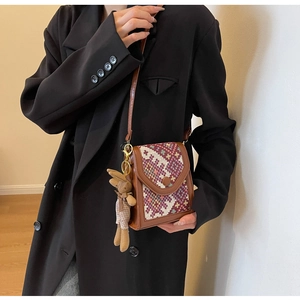 Detail of vintage patterned crossbody bag with plush rabbit charm and brown leather trim