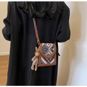 Detailed side view of an ethnic style crossbody bag with a plush bunny charm on a model