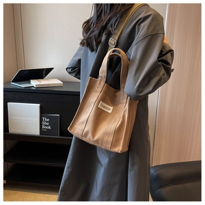 Detail of coffee canvas tote with FASHION label and adjustable green strap on model