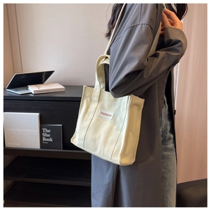 Detail of beige canvas tote with stitched FASHION label and adjustable shoulder strap