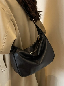 Classic black leather hobo bag with gold zipper shown on model in a stylish trench coat