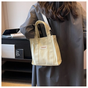 Detail of minimalist canvas tote with adjustable strap worn over a dark winter coat